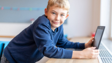 Pojke med blå tröja i årskurs tre med en dator framför sig .