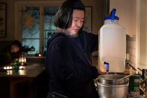 Kvinna håller en vattendunk med tappkran över en kastrull som står på spisen.