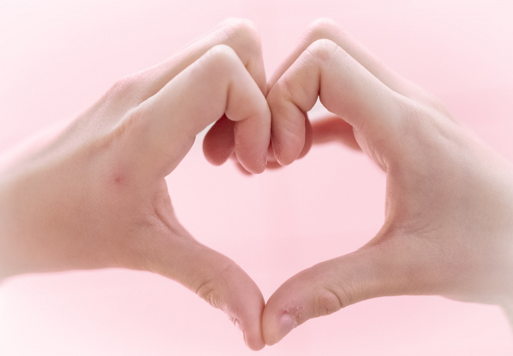 Två händer formar ett hjärta mot en rosa bakgrund.