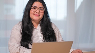 Kvinna sitter vid sin dator och ler mot kameran.